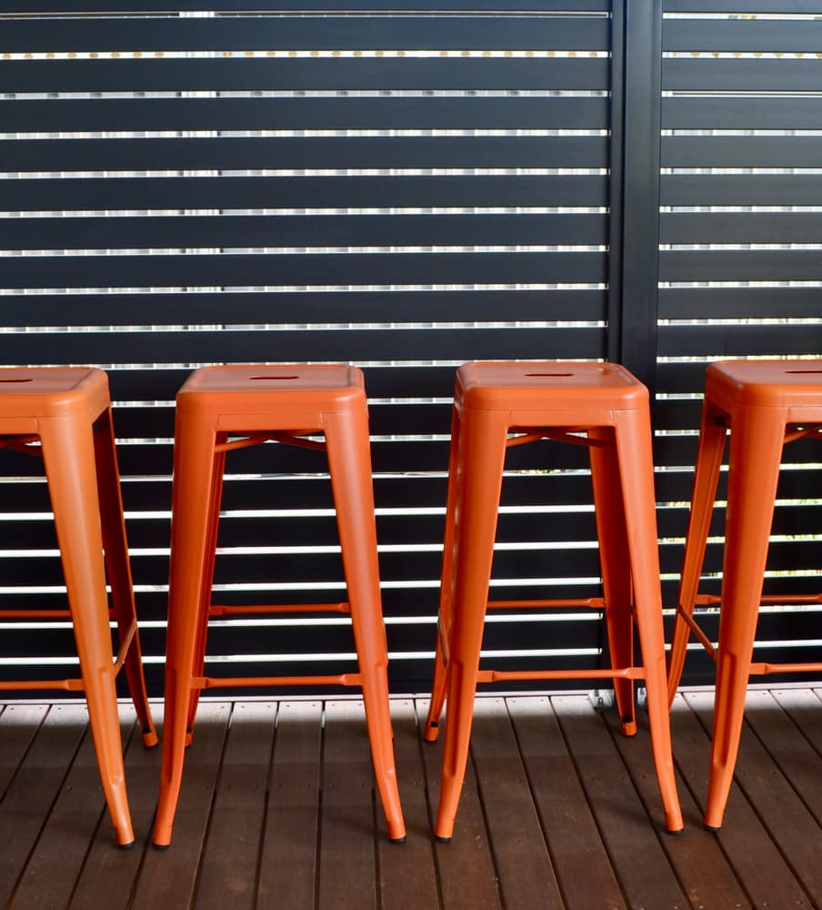 Four Orange Bar Stools Are Lined Up In Front Of A Black Fence — A Betta Fence 'N' Yard In Port Macquarie, NSW