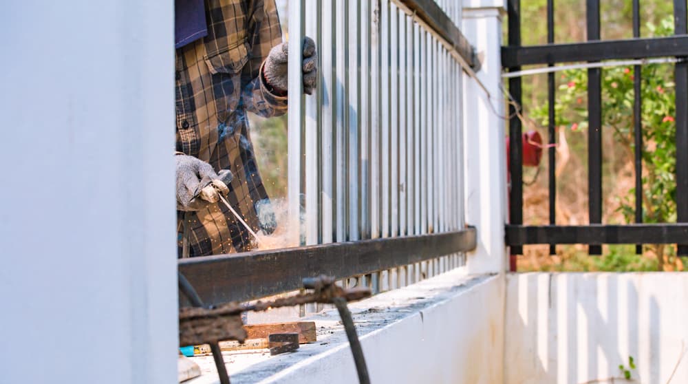 A Man Is Welding A Metal Fence With A Welding Machine — A Betta Fence 'N' Yard In Port Macquarie, NSW