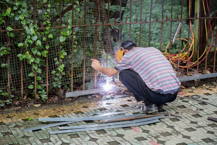A Man Is Welding A Metal Fence With A Welding Machine — A Betta Fence 'N' Yard In Port Macquarie, NSW