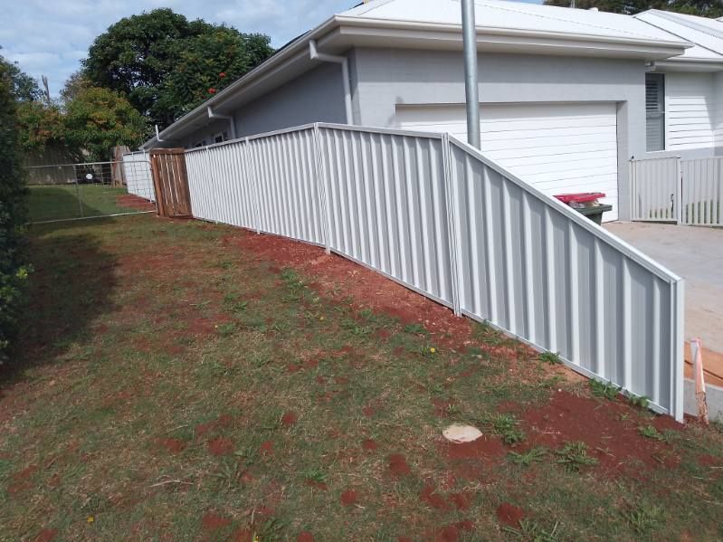 A White Fence Surrounds A Grassy Hillside In Front Of A House — A Betta Fence 'N' Yard In Port Macquarie, NSW