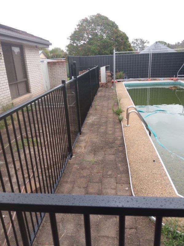 A Fence Surrounds A Swimming Pool With A House In The Background — A Betta Fence 'N' Yard In Port Macquarie, NSW