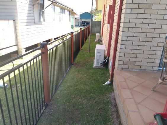 A Fence Surrounds A Grassy Area Next To A Brick Building — A Betta Fence 'N' Yard In Thrumster, NSW