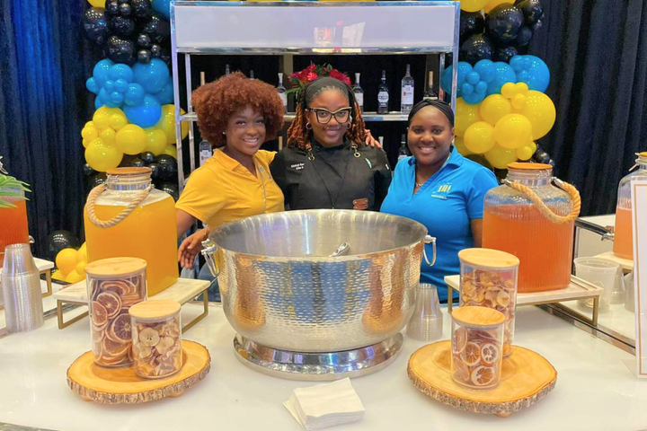 Three women are posing for a picture in front of a table filled with drinks.