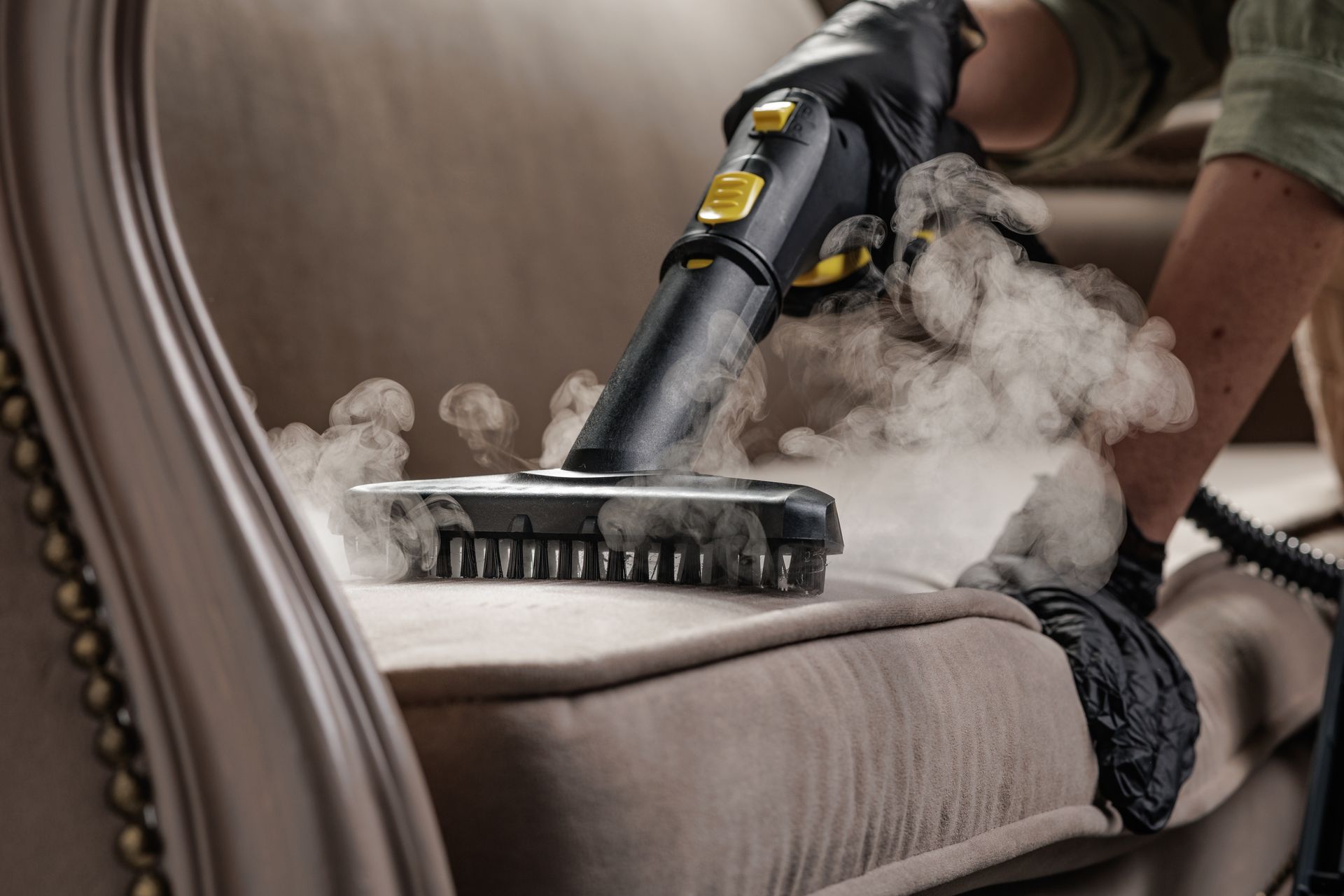Steam cleaner being used on a beige sofa, releasing steam.