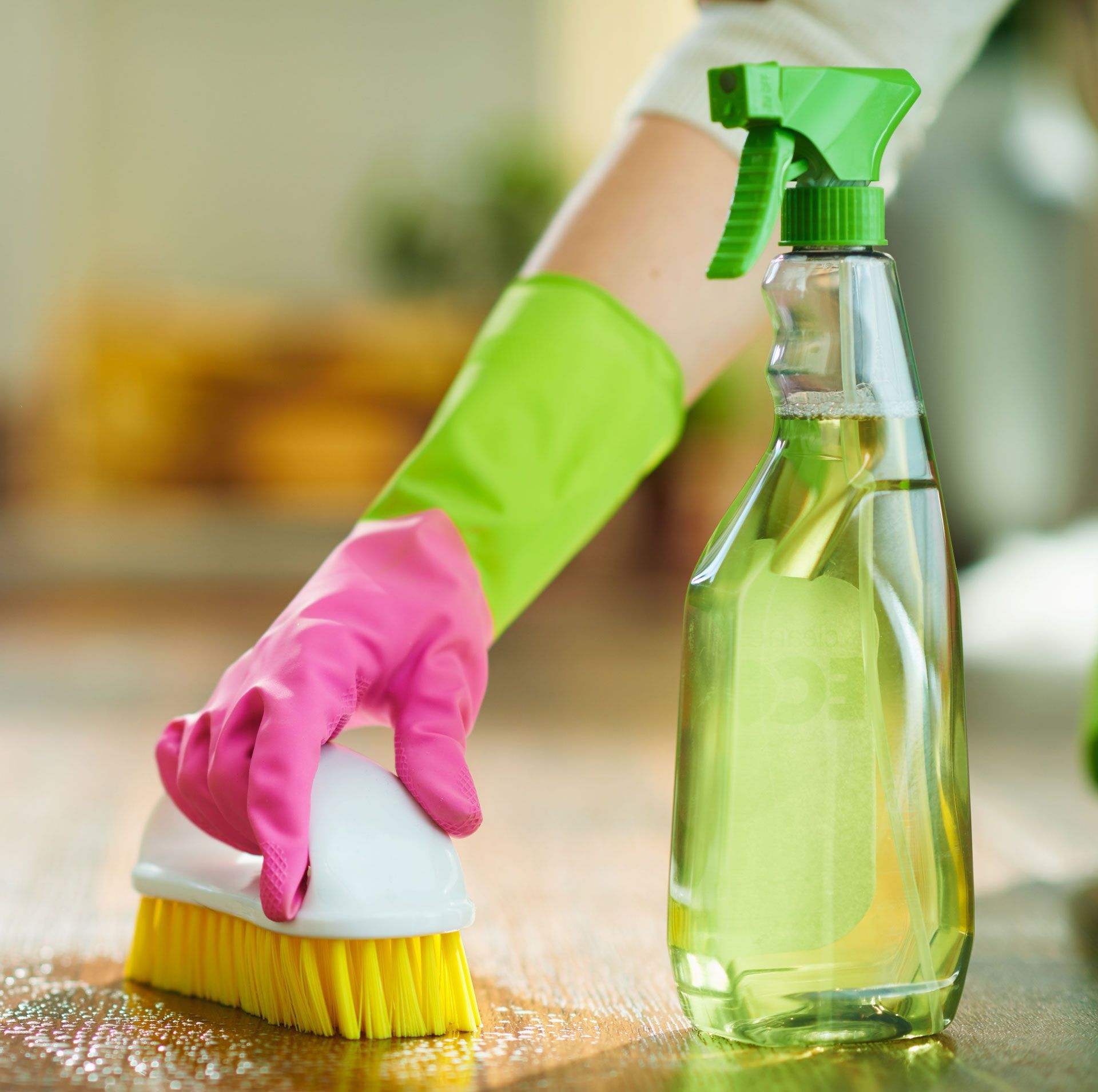 Person wearing gloves cleans a surface with a brush and spray bottle.