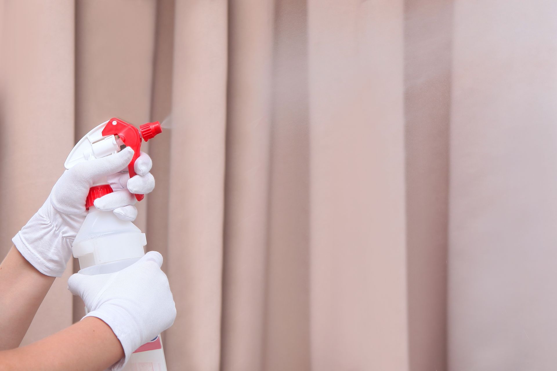 Person in gloves sprays curtains with a red and white spray bottle.