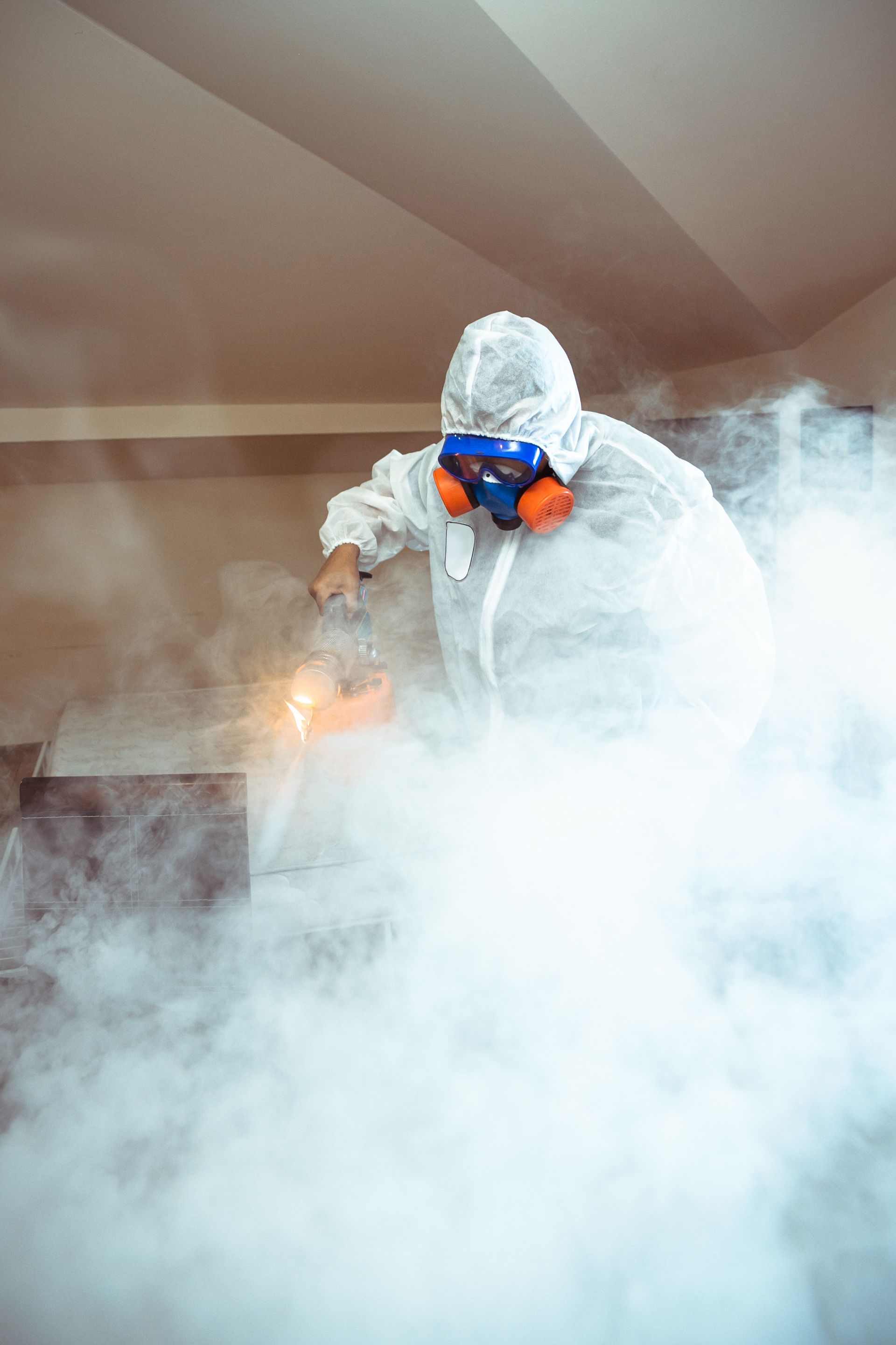 Person in protective suit, respirator, spraying disinfectant, surrounded by fog on a staircase.