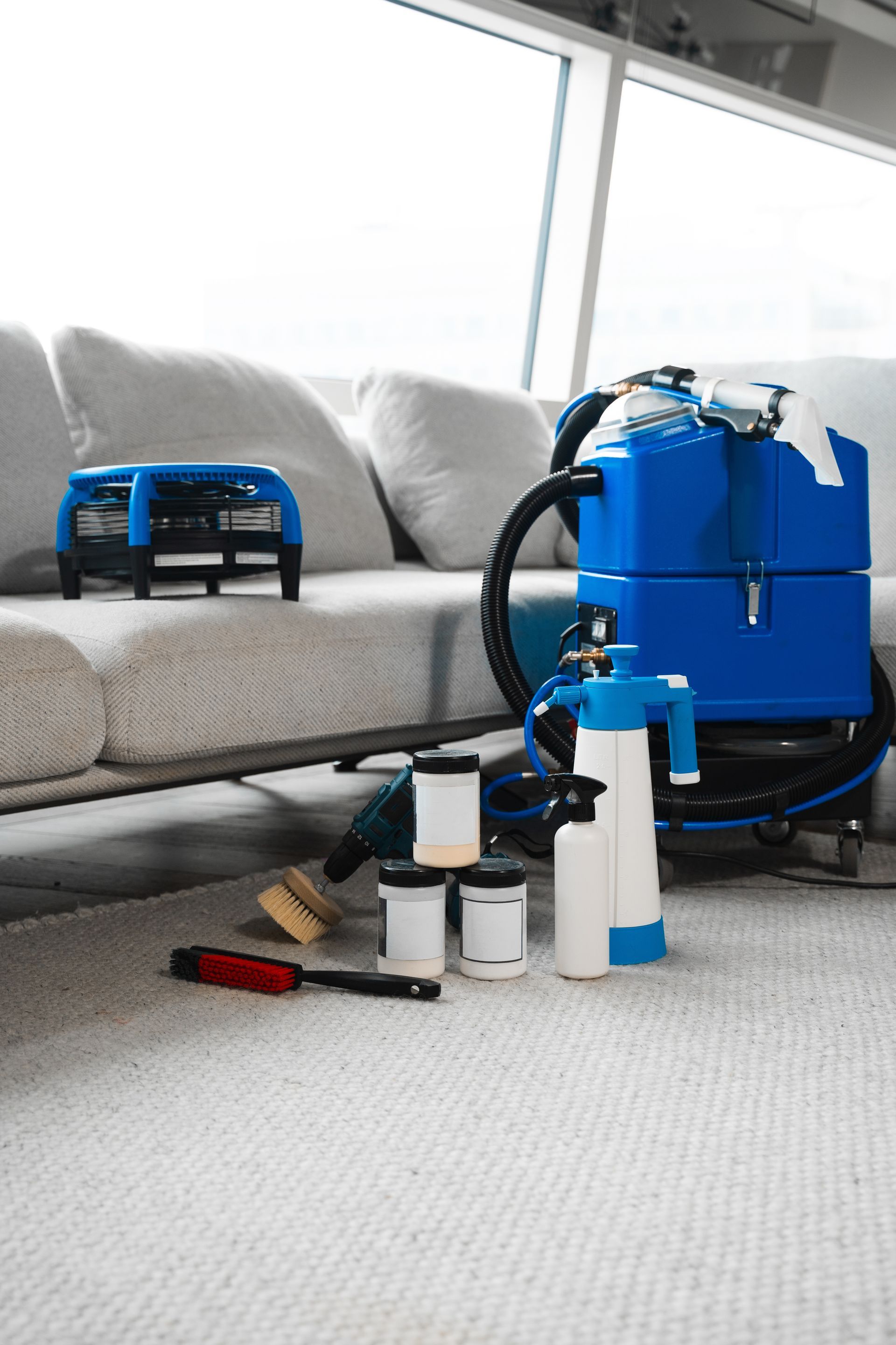 Blue carpet cleaning machine and supplies on a rug near a sofa.