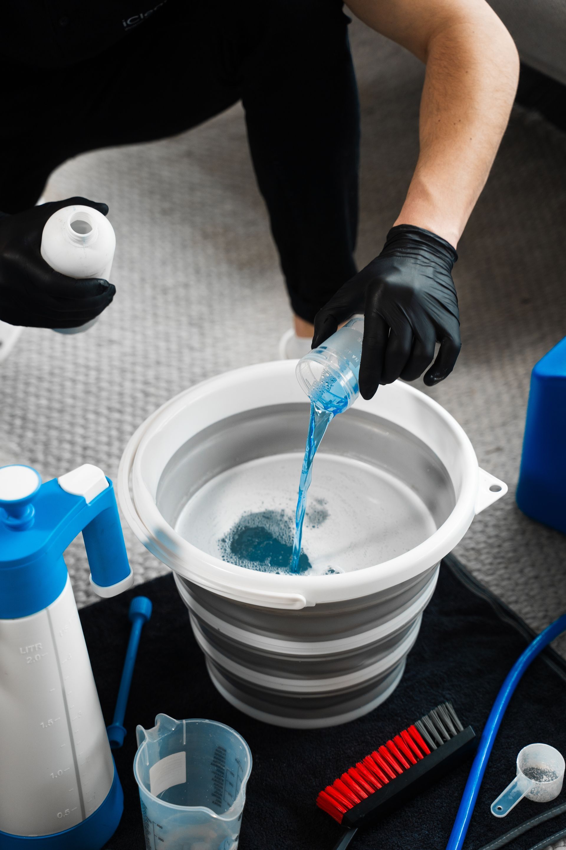 Person pouring blue liquid into a bucket, surrounded by cleaning supplies.