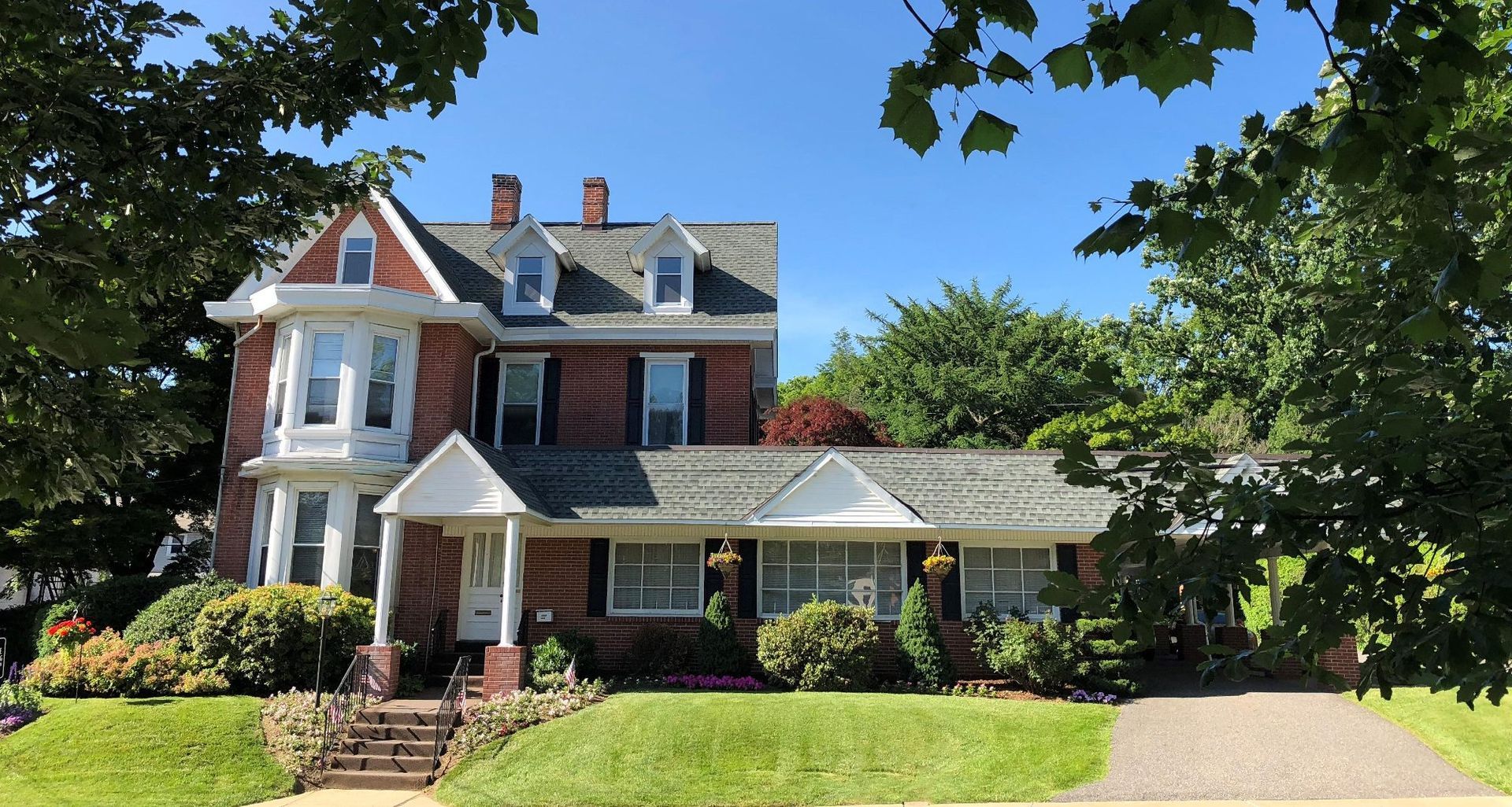 Large Victorian-style house with red brick, white trim, and a green lawn under a sunny blue sky
