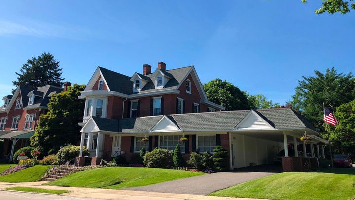 Large red-brick house with white trim, covered porch, manicured lawn, and an American flag on a sunny day