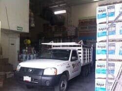 Un camión blanco de plataforma estaba estacionado dentro de un almacén junto a pilas de cajas de materiales de construcción.