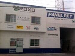 Un edificio comercial de varias plantas con paredes blancas, detalles en azul y letreros de Roxo y Panel Rey.