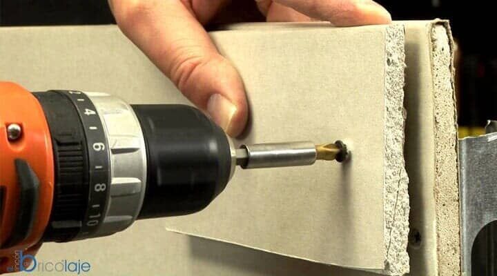 Una persona utiliza un taladro eléctrico para atornillar un tornillo en un trozo de panel de yeso fijado a un montante metálico.
