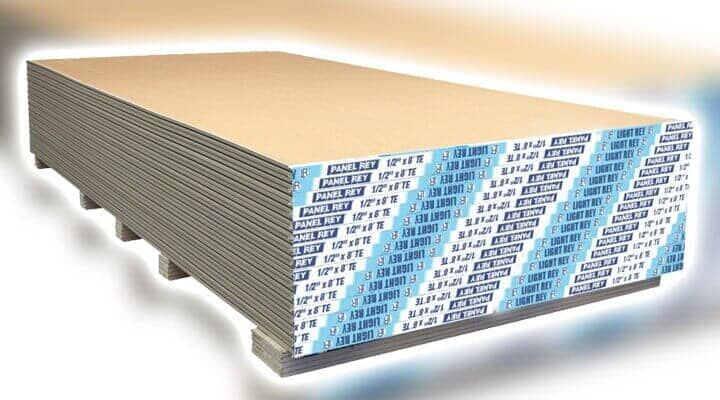 Una pila de láminas de paneles de yeso con texto de marca en azul en un lateral, apoyadas sobre separadores de madera.