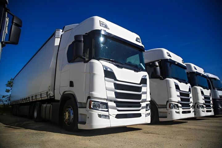 A row of white semi trucks parked next to each other in a parking lot.