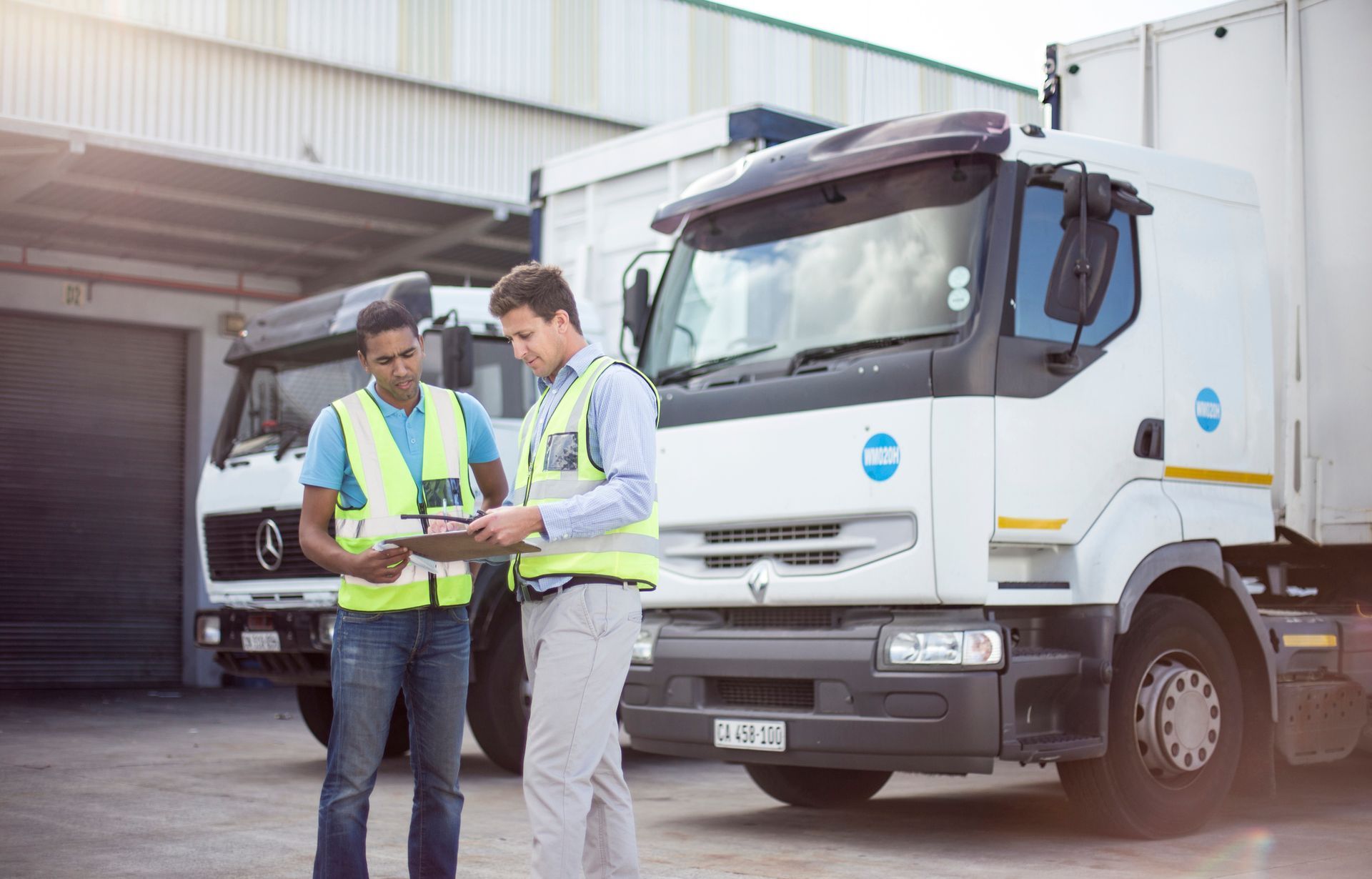 Two men are standing in front of a truck looking at a clipboard.