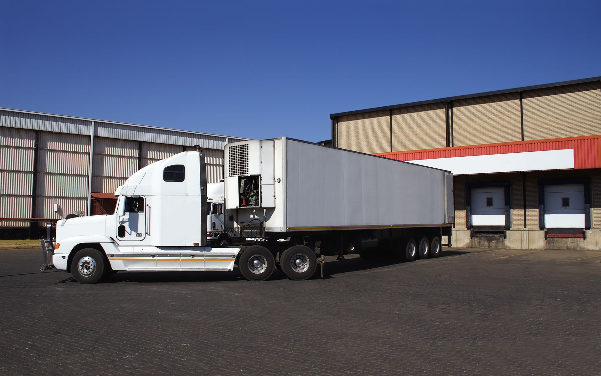 A white semi truck is parked in front of a warehouse.