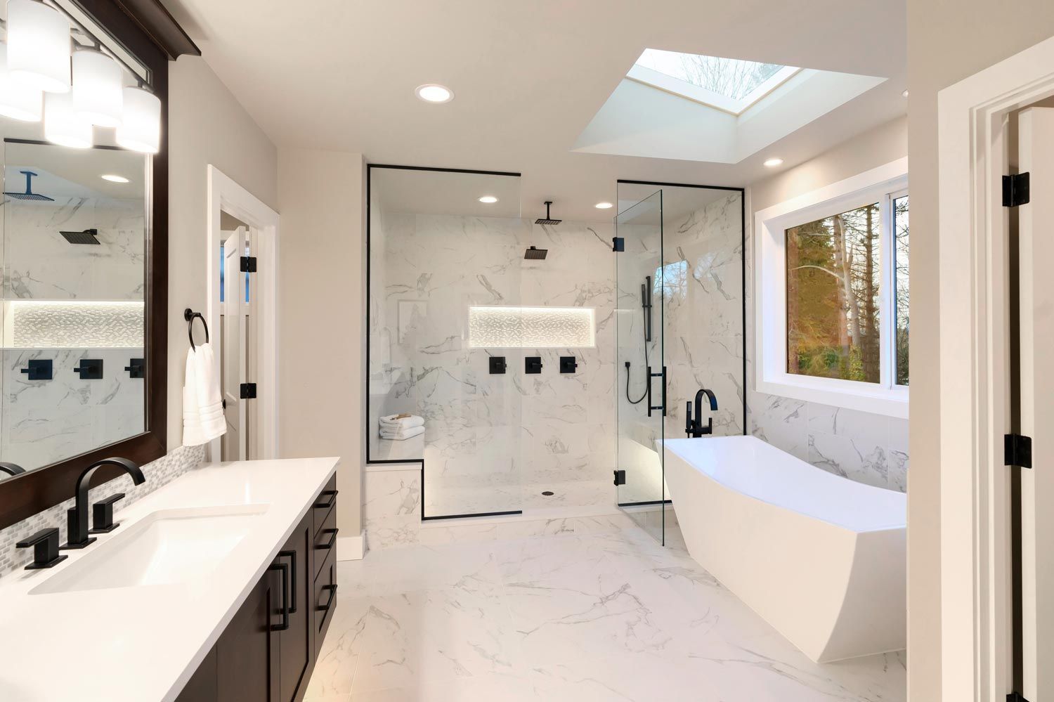 Bright modern bathroom with double vanity, glass shower, freestanding tub, and large window