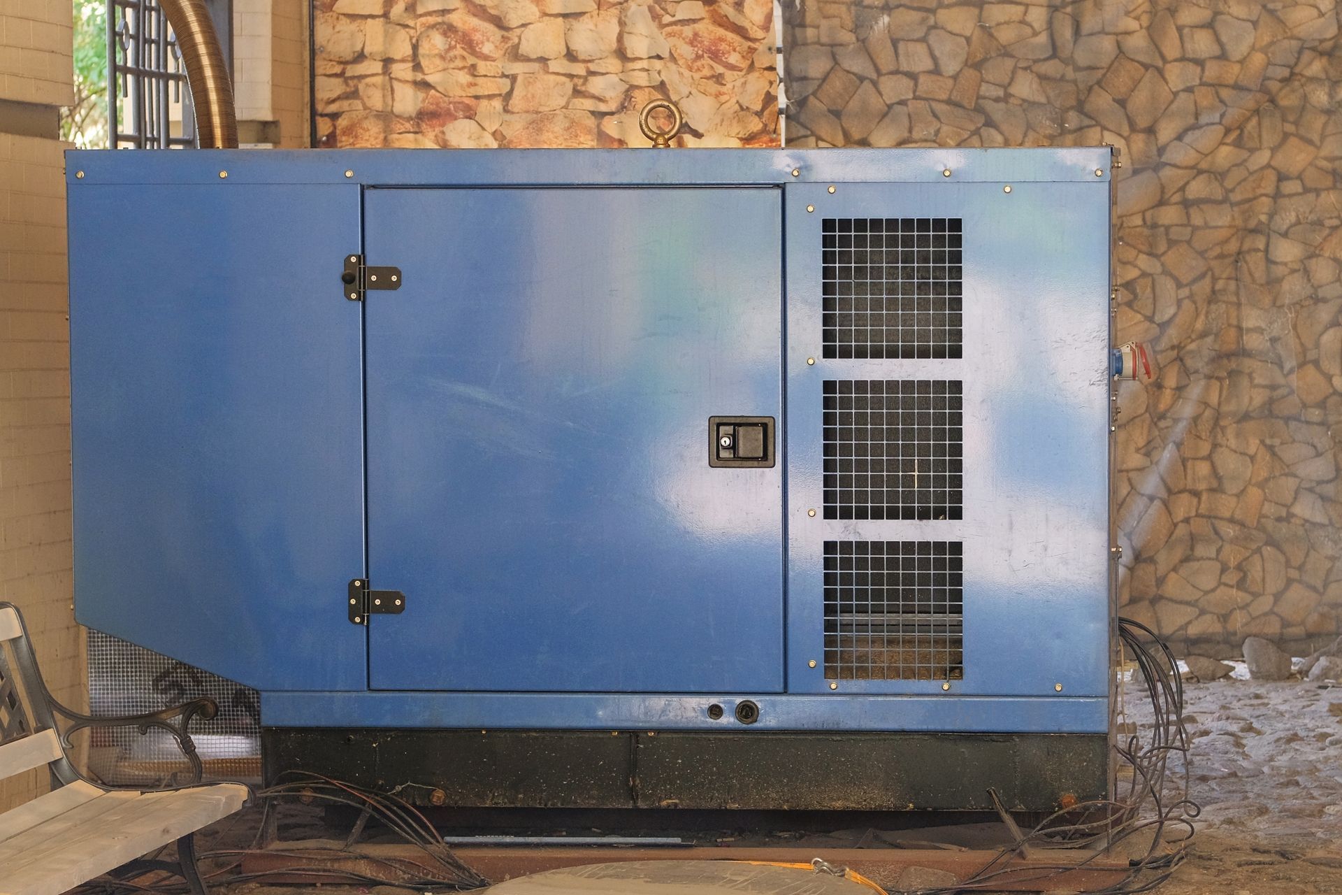 Blue generator with a closed door, vent, and handle, on a platform.