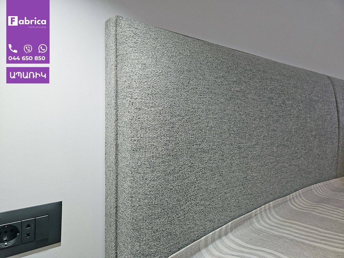 A bed with a gray headboard and a purple sign on the wall.