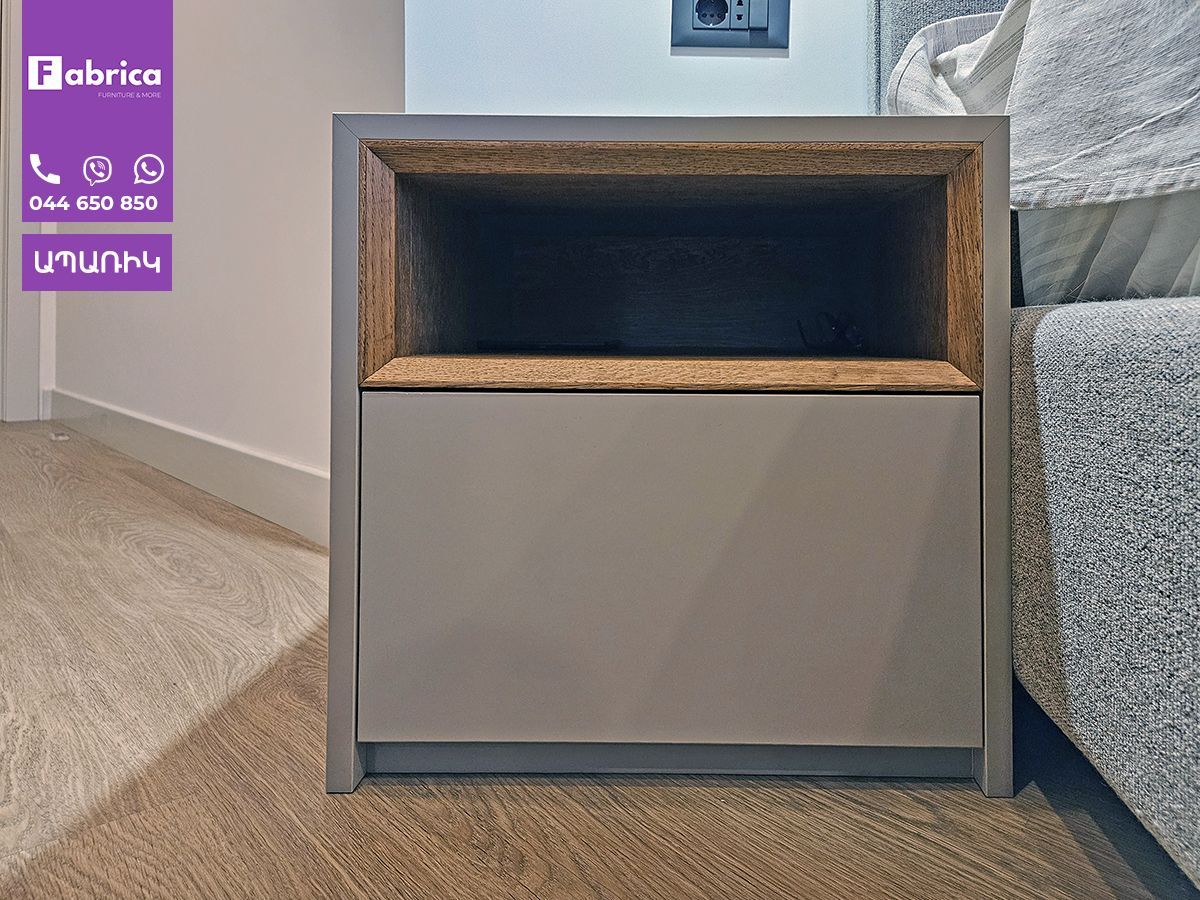 A nightstand is sitting next to a bed in a bedroom.