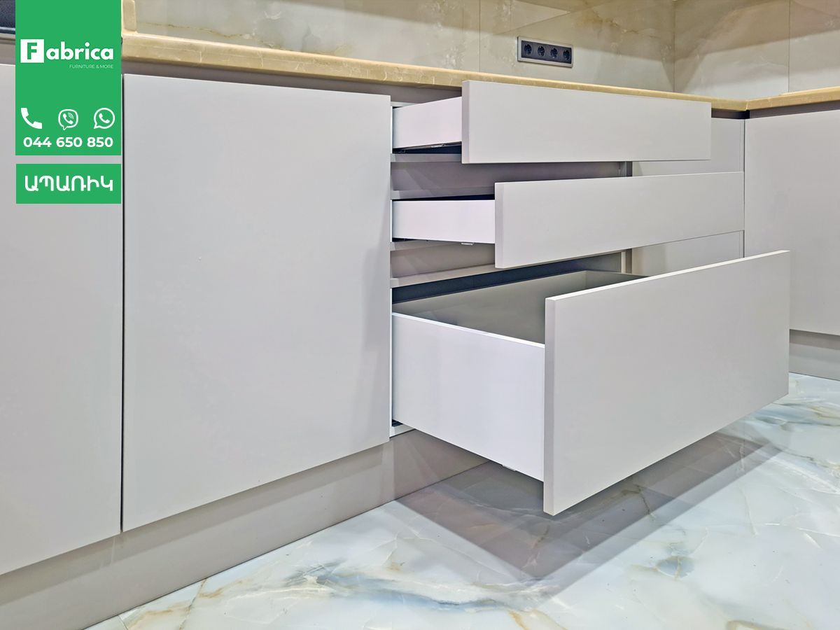 A kitchen with white cabinets and drawers with the drawer open.