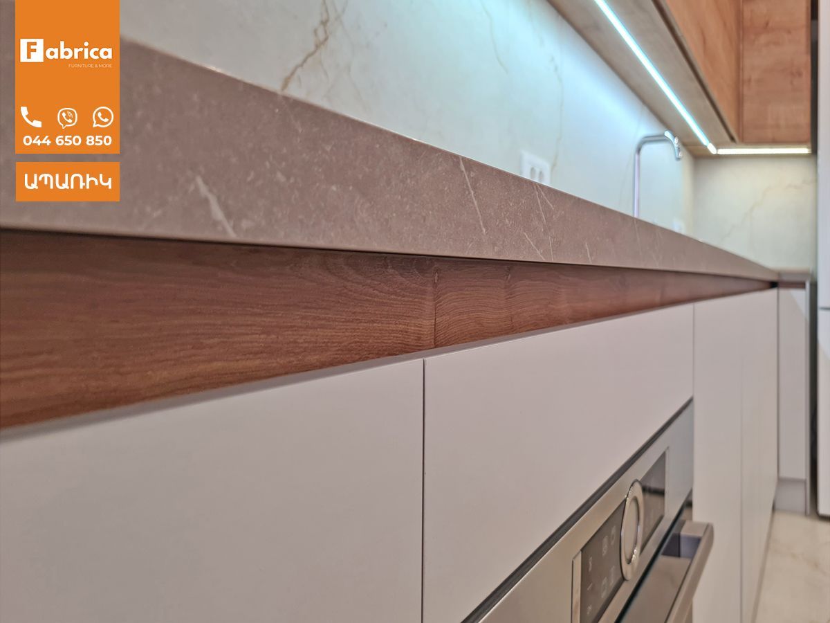 A kitchen with white cabinets and wooden handles and a stainless steel oven.