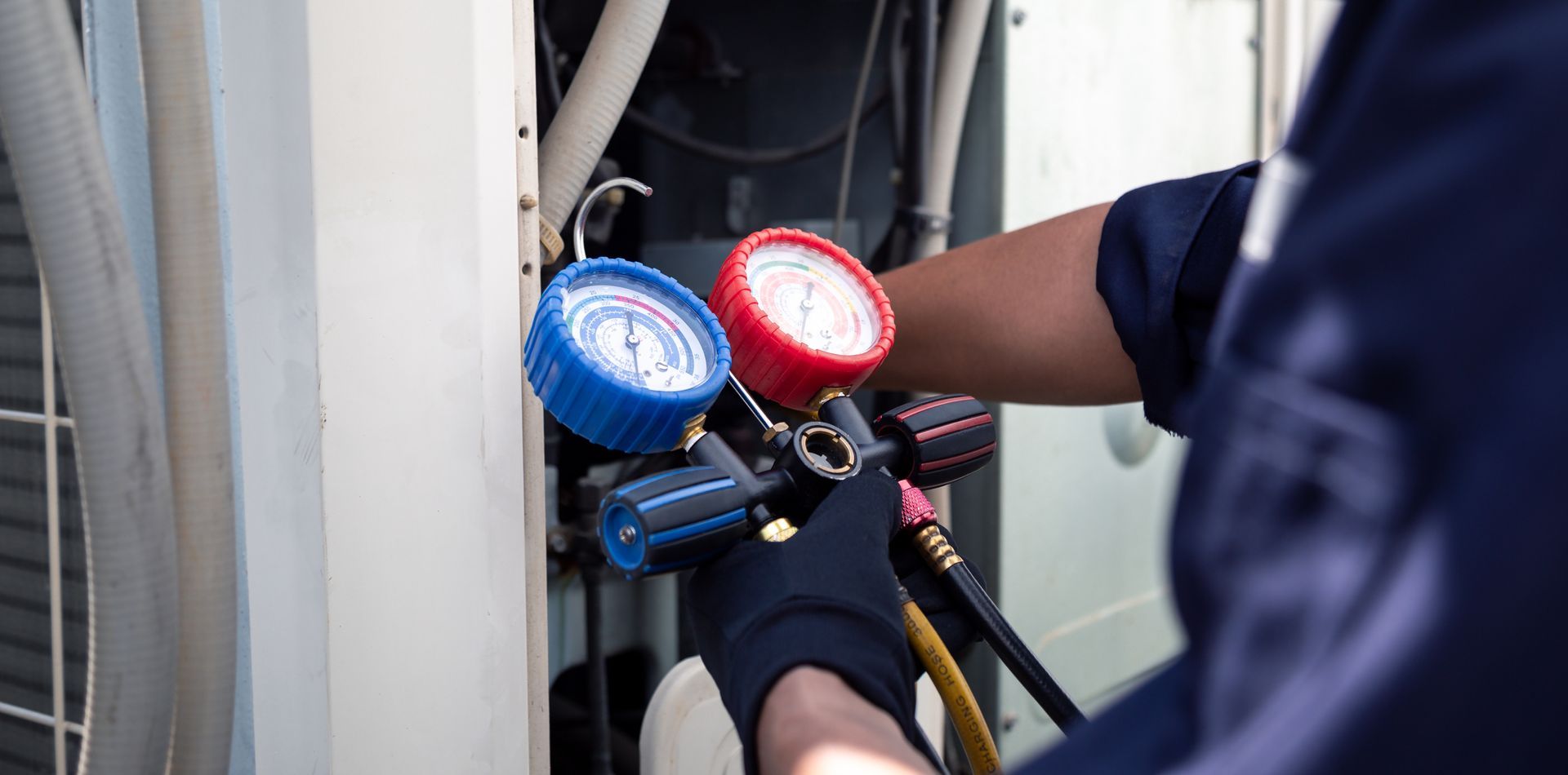 Person wearing gloves using gauges on an HVAC unit, checking pressure.