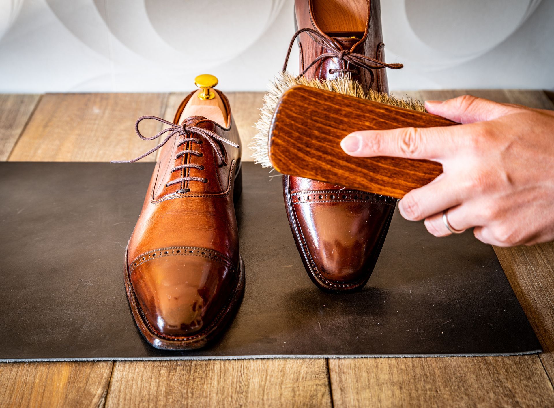 A person is polishing a pair of brown shoes with a brush.
