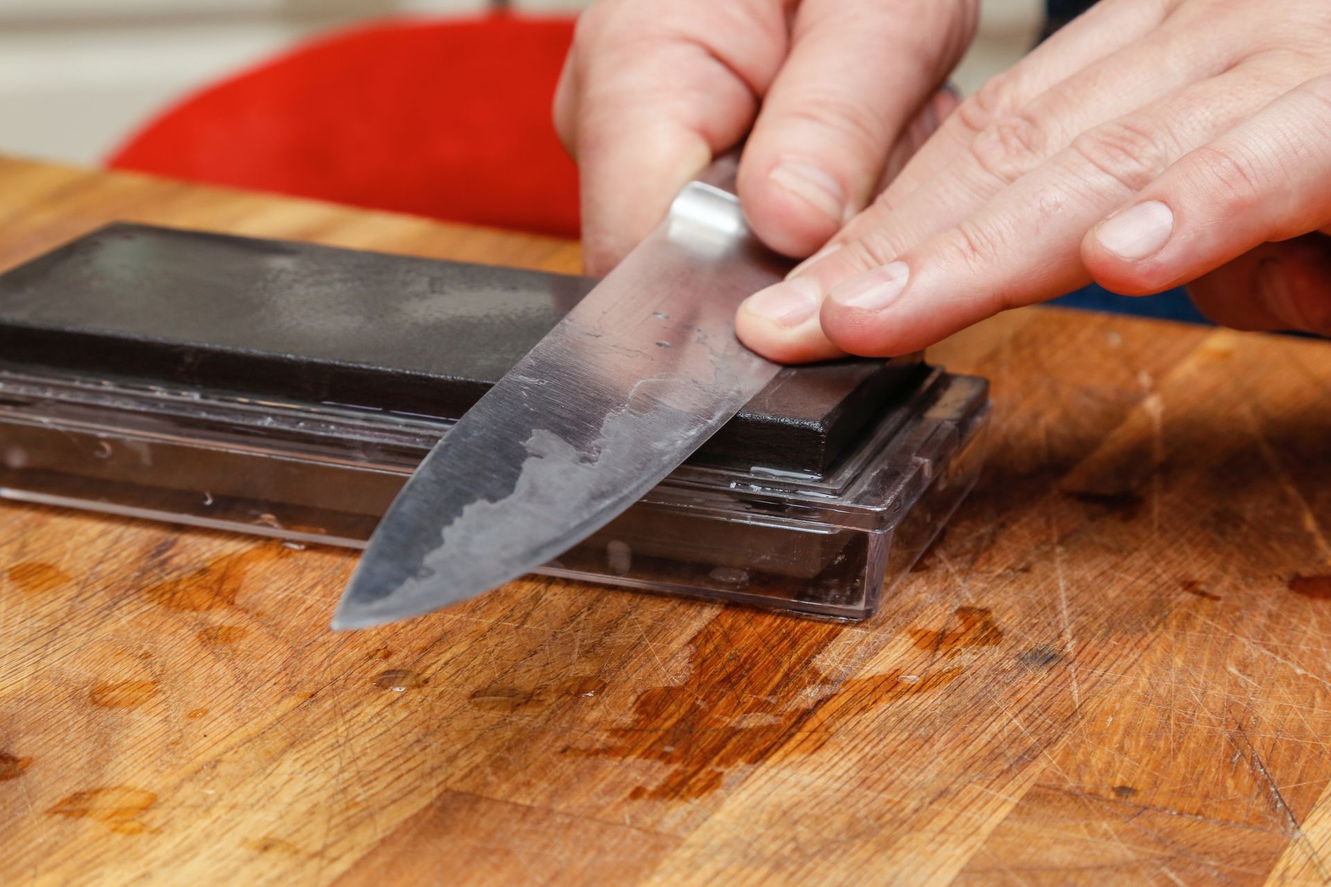 A hand sharpening a knife on a whetstone placed on a wooden surface.