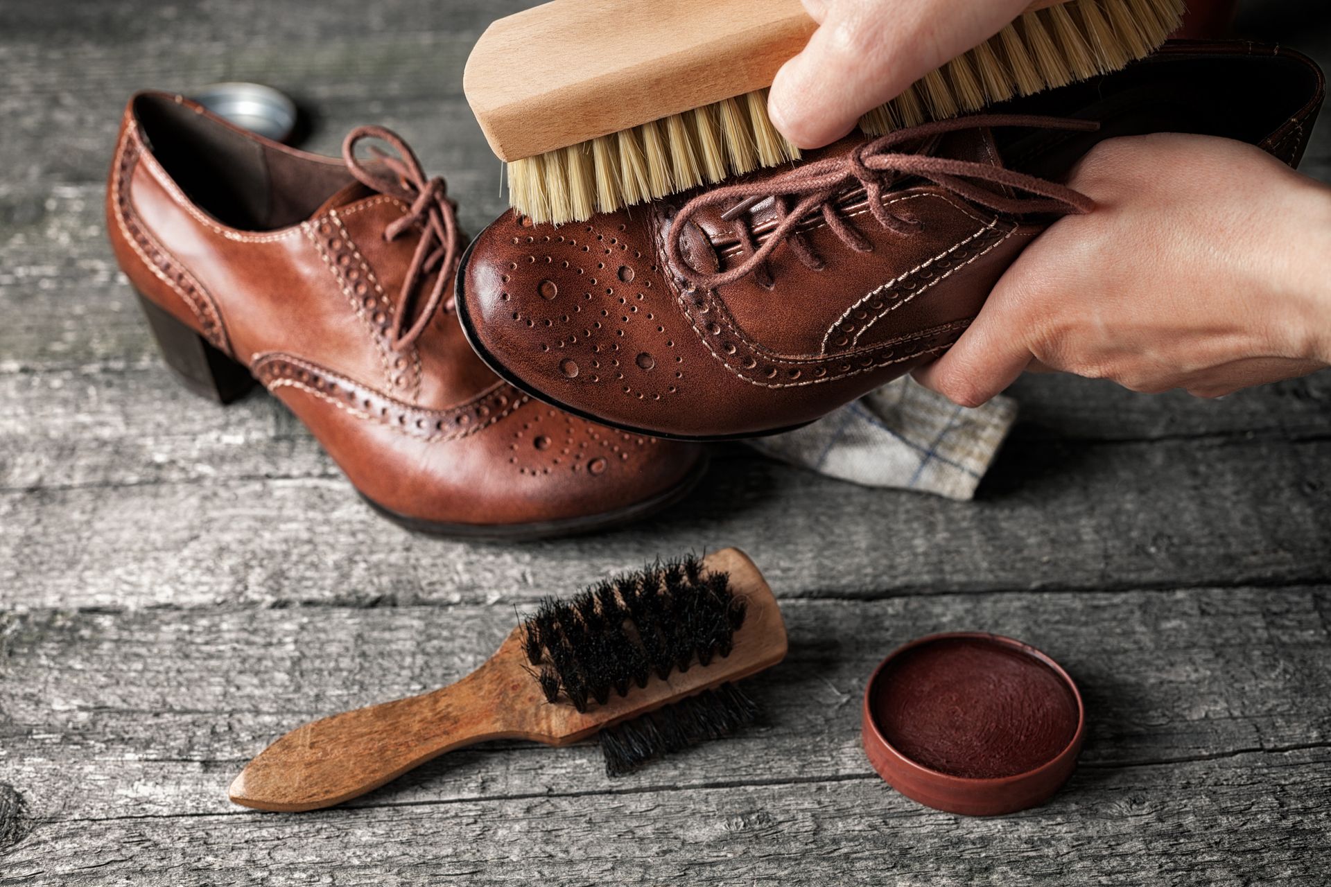 A person is cleaning a pair of brown shoes with a brush.
