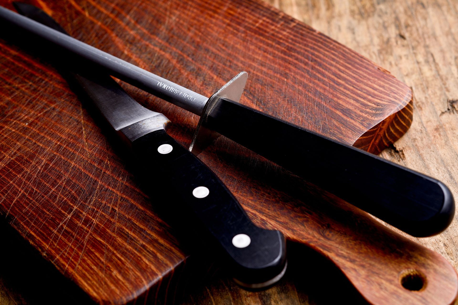 A chef's knife with a black handle and a honing steel resting on a wooden surface.