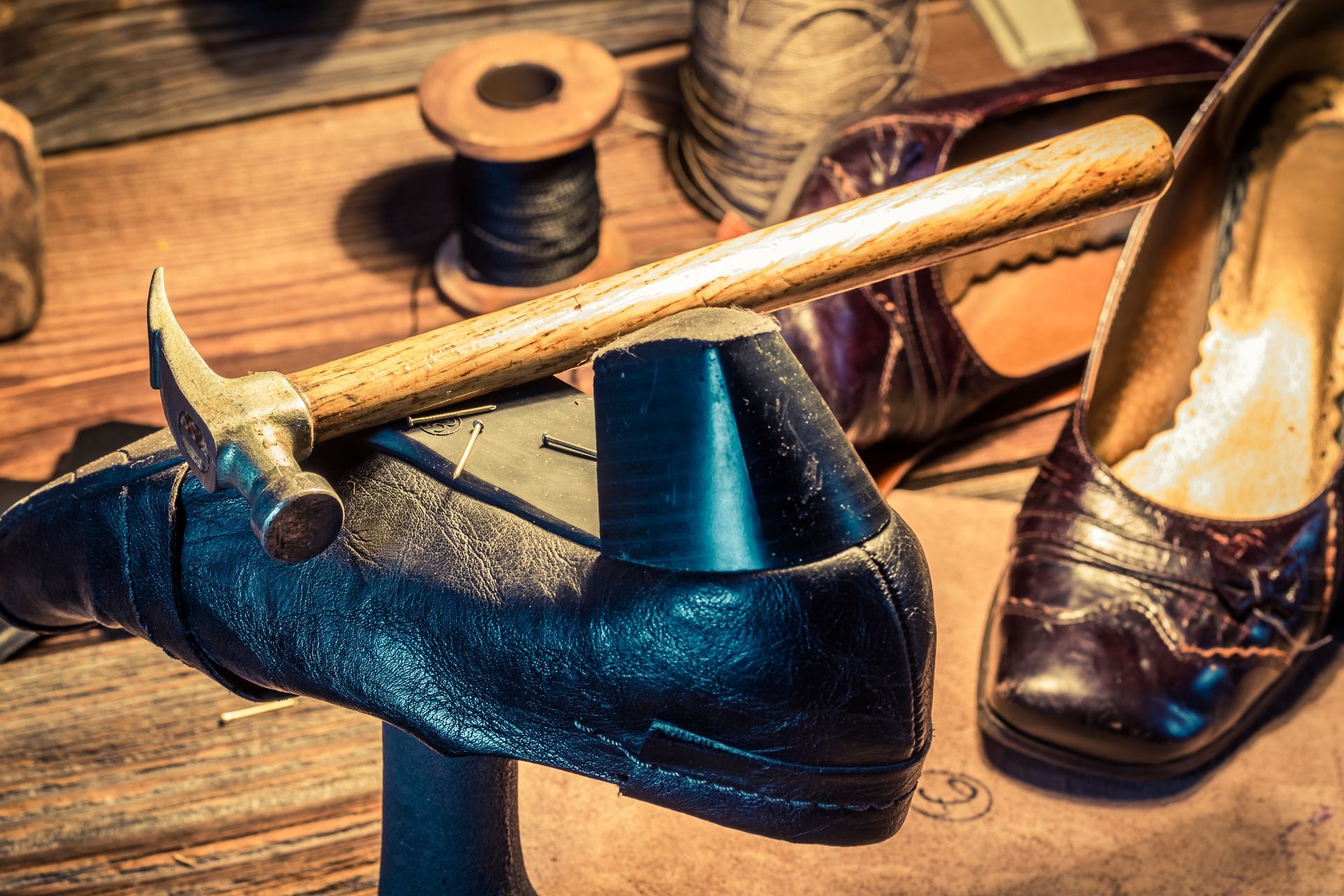 A hammer is sitting on top of a shoe on a wooden table.