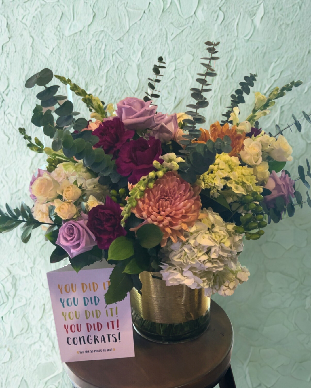 Bouquet of flowers filled with white and purple roses, snapdragons, and eucalyptus, plus a congratulations card