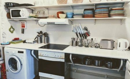 A kitchen with a washer and dryer , stove , microwave , and shelves.