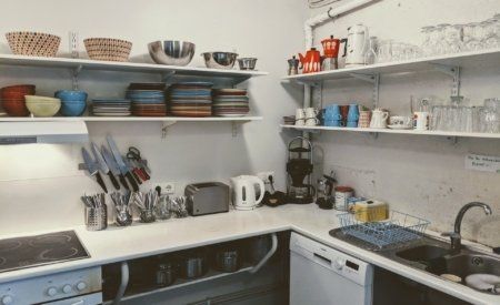 A kitchen with a sink , stove , dishwasher , and shelves filled with bowls and plates.