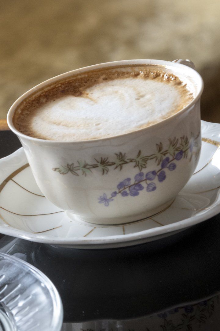 A cup of coffee on a saucer with purple flowers on it