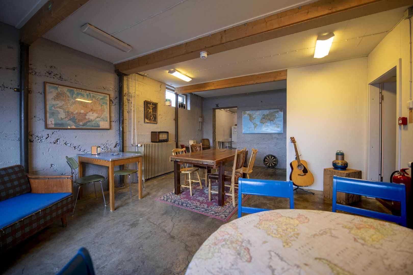 A living room with a table , chairs , a guitar and a map on the wall.