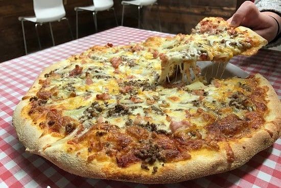 A person is taking a slice of pizza from a pizza on a checkered table cloth.