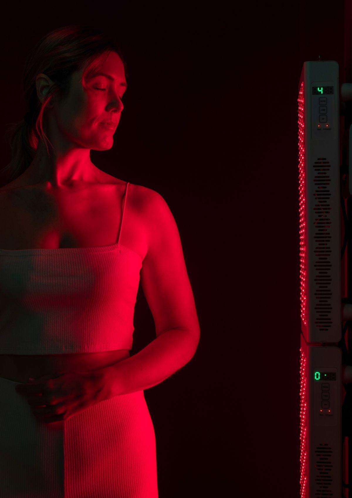 Woman standing near red LED light panel, illustrating benefits of red light therapy for skin in Albuquerque.