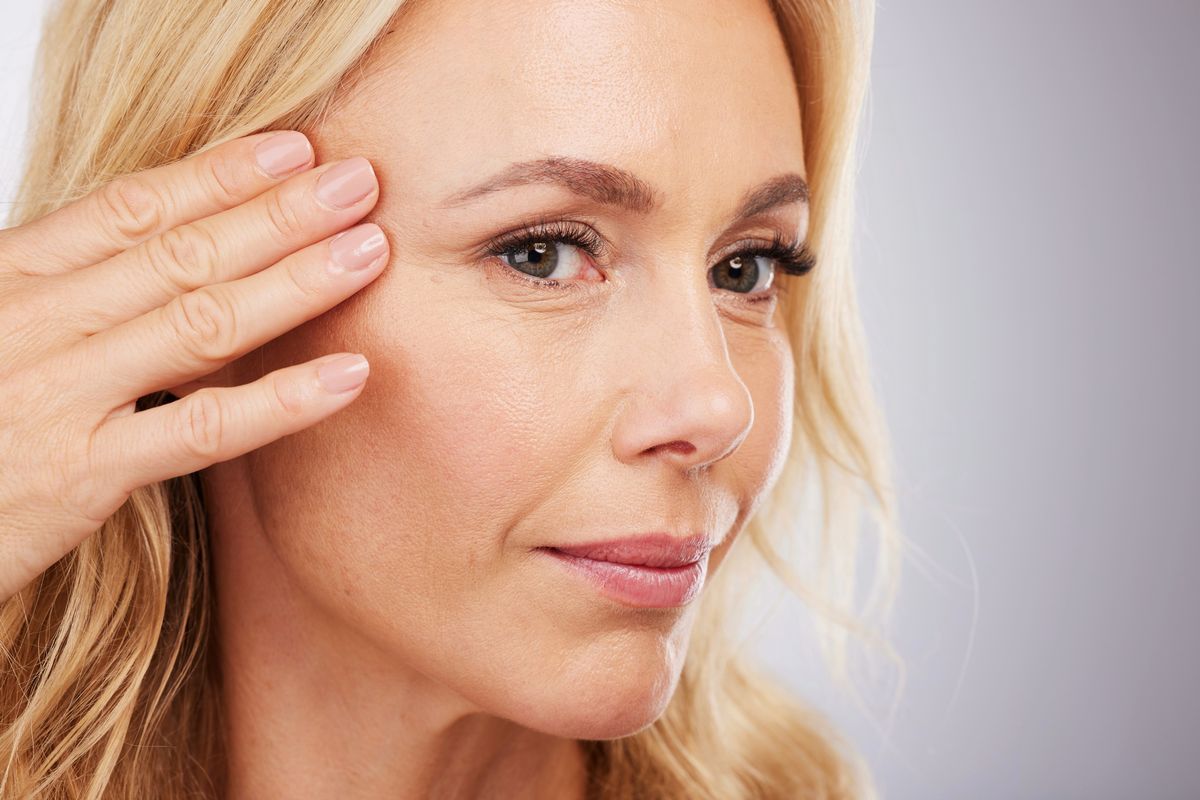 Blonde woman touching her face, illustrating DermaFrac microneedling facial treatment for smoother skin in Albuquerque.