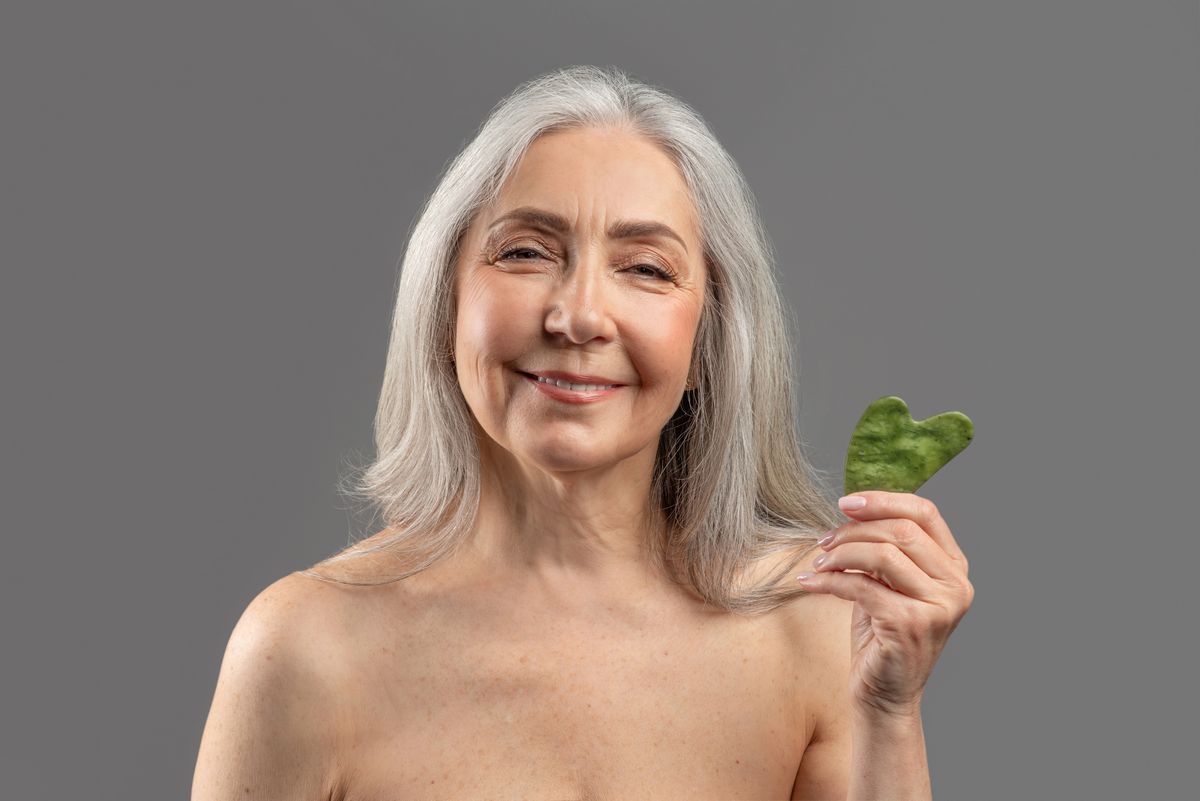 Smiling woman holding Gua Sha stone, representing Sculpting Facial with cupping, Kansa, and massage therapy in Albuquerque.