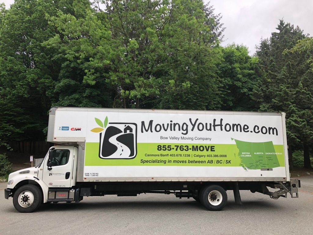 A moving truck is parked in a parking lot with trees in the background.