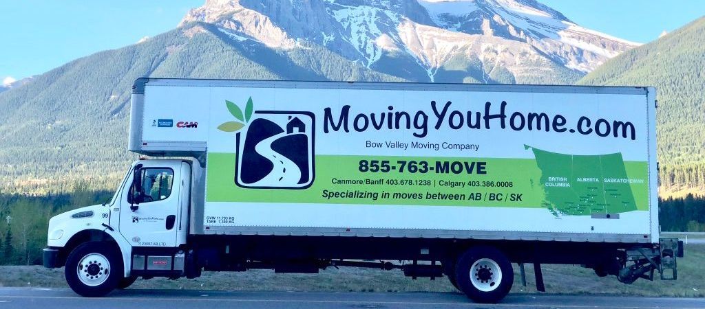 A moving truck is parked on the side of the road in front of a mountain.