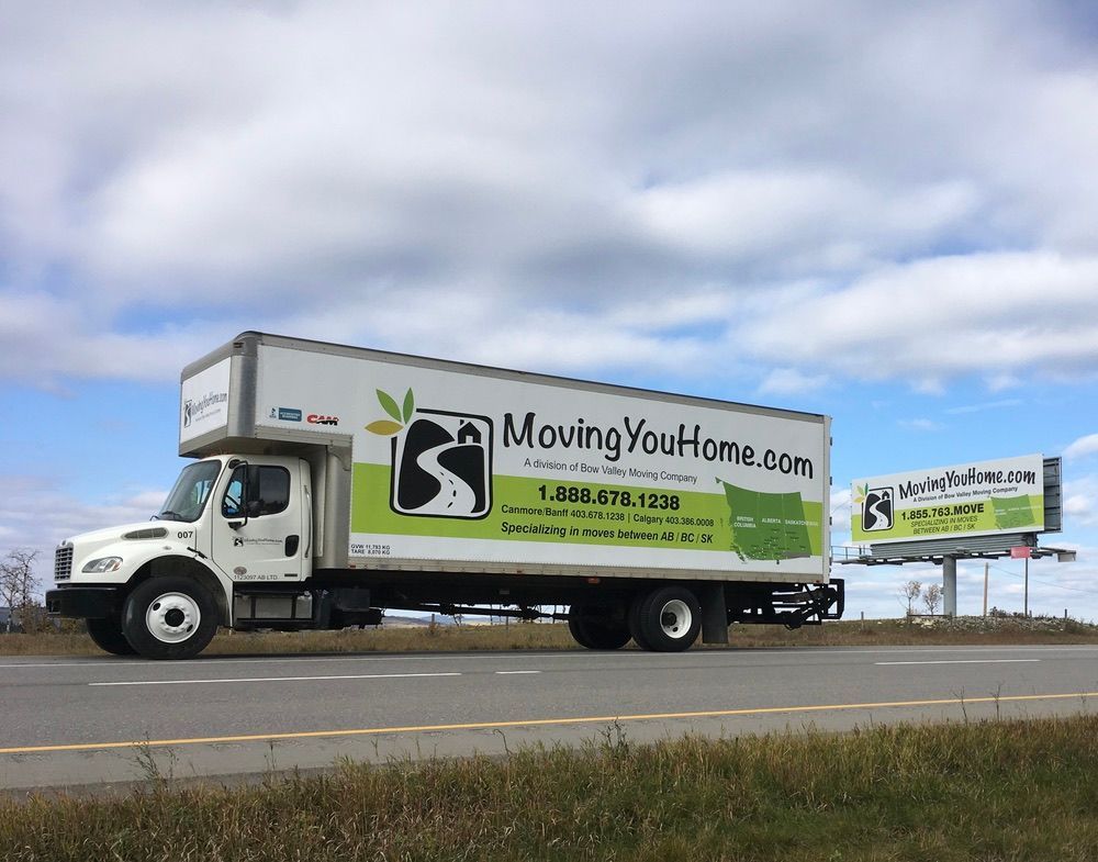 A moving truck is driving down a highway next to a billboard.
