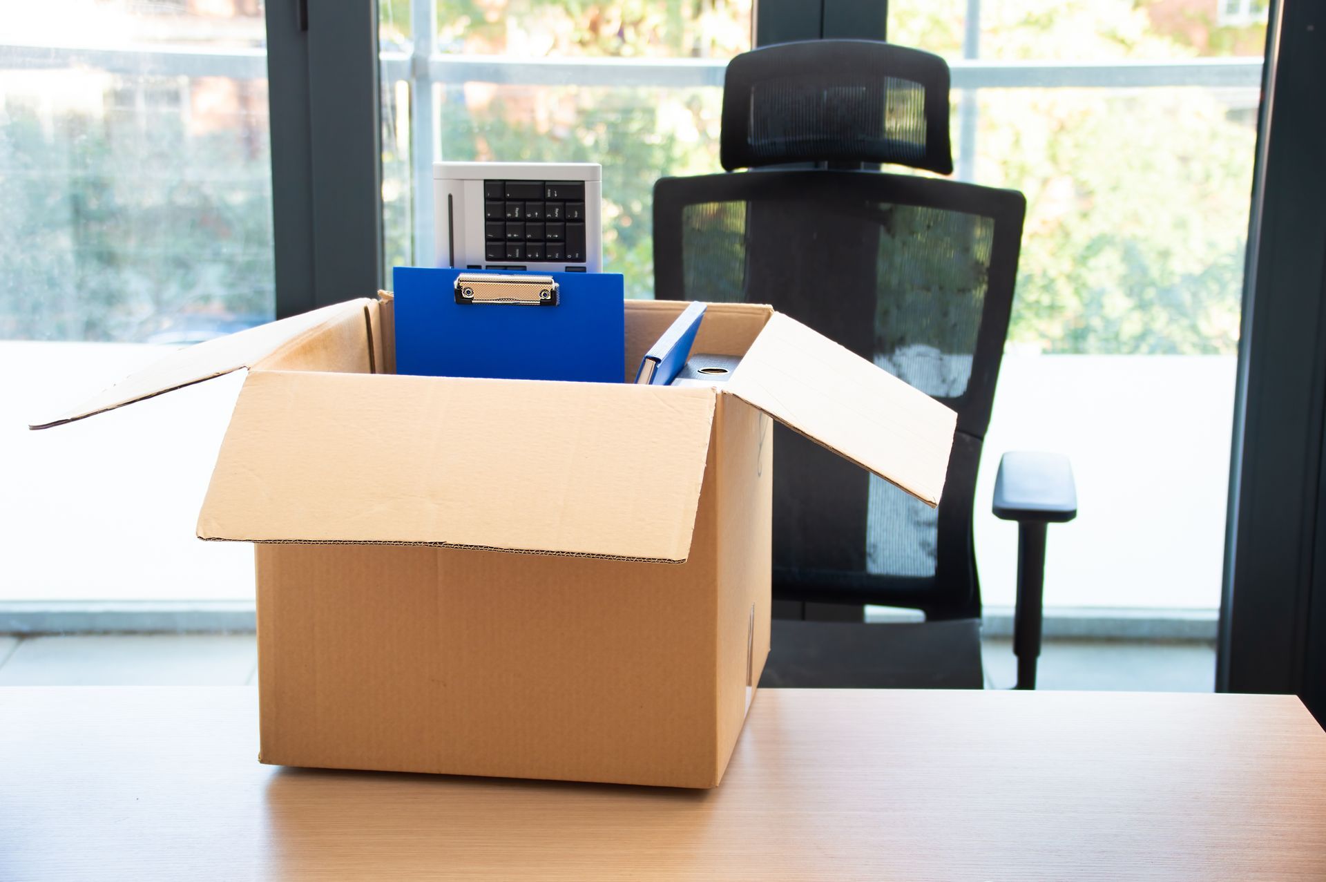 Cardboard box filled with office supplies on a desk, office chair in background.