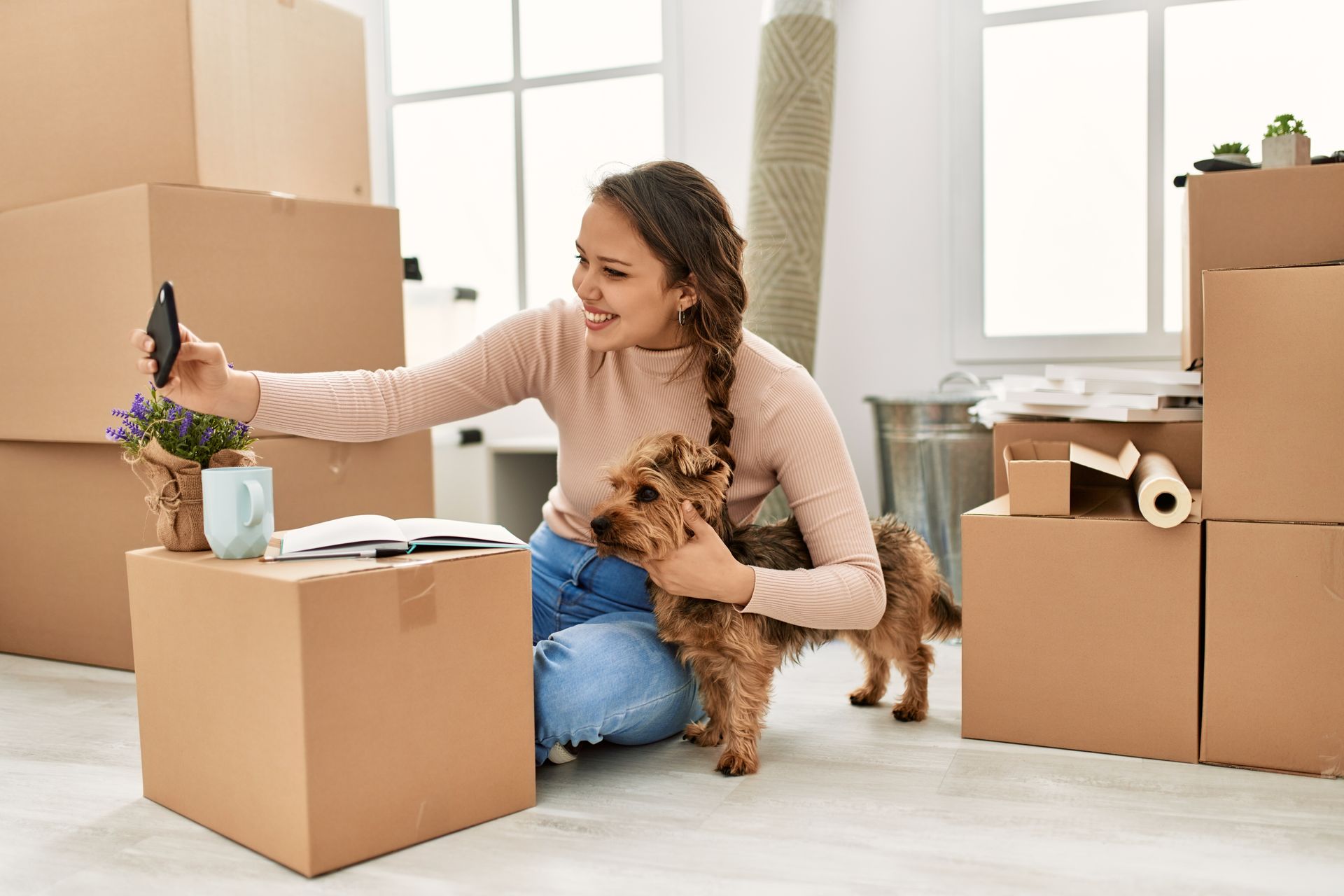 Woman takes selfie with dog in a room filled with moving boxes.