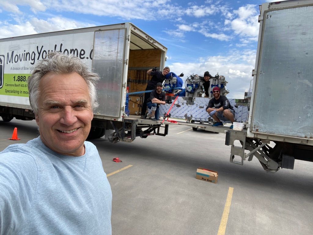 A man is taking a selfie in front of a moving truck.