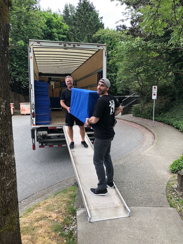 Two men are loading a blue couch into a moving truck.